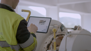 Ship engineer performing check on a winch and filling a digital form on a portable device