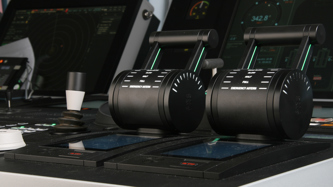 Close-up of a ship’s control console with two black throttle levers mounted side by side on a rectangular base.