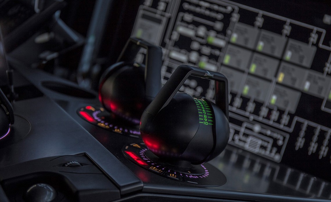 Close-up of two joystick-style control levers mounted on a dark console, each surrounded by illuminated circular indicators in red and purple tones.