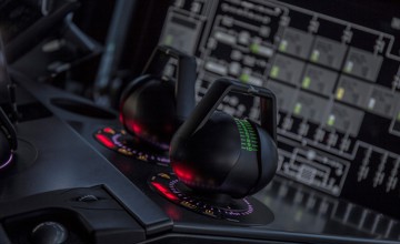 Close-up of two joystick-style control levers mounted on a dark console, each surrounded by illuminated circular indicators in red and purple tones. 