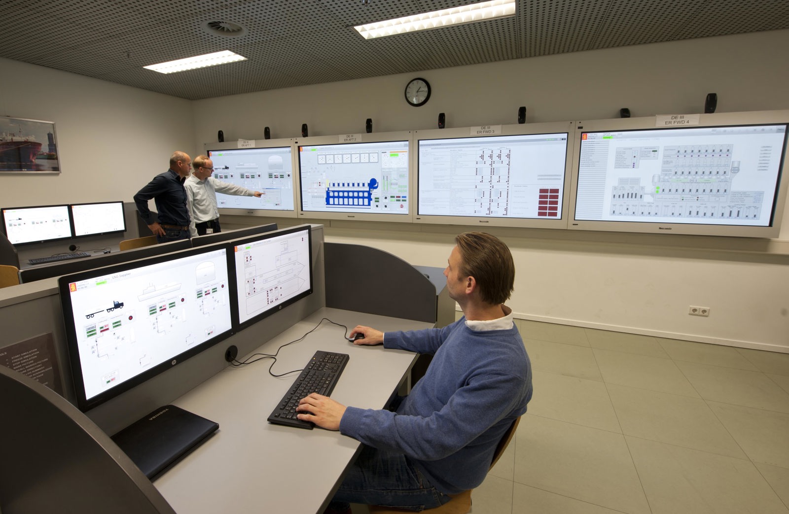 A modern control room where one person sits at a desk operating dual computer monitors
