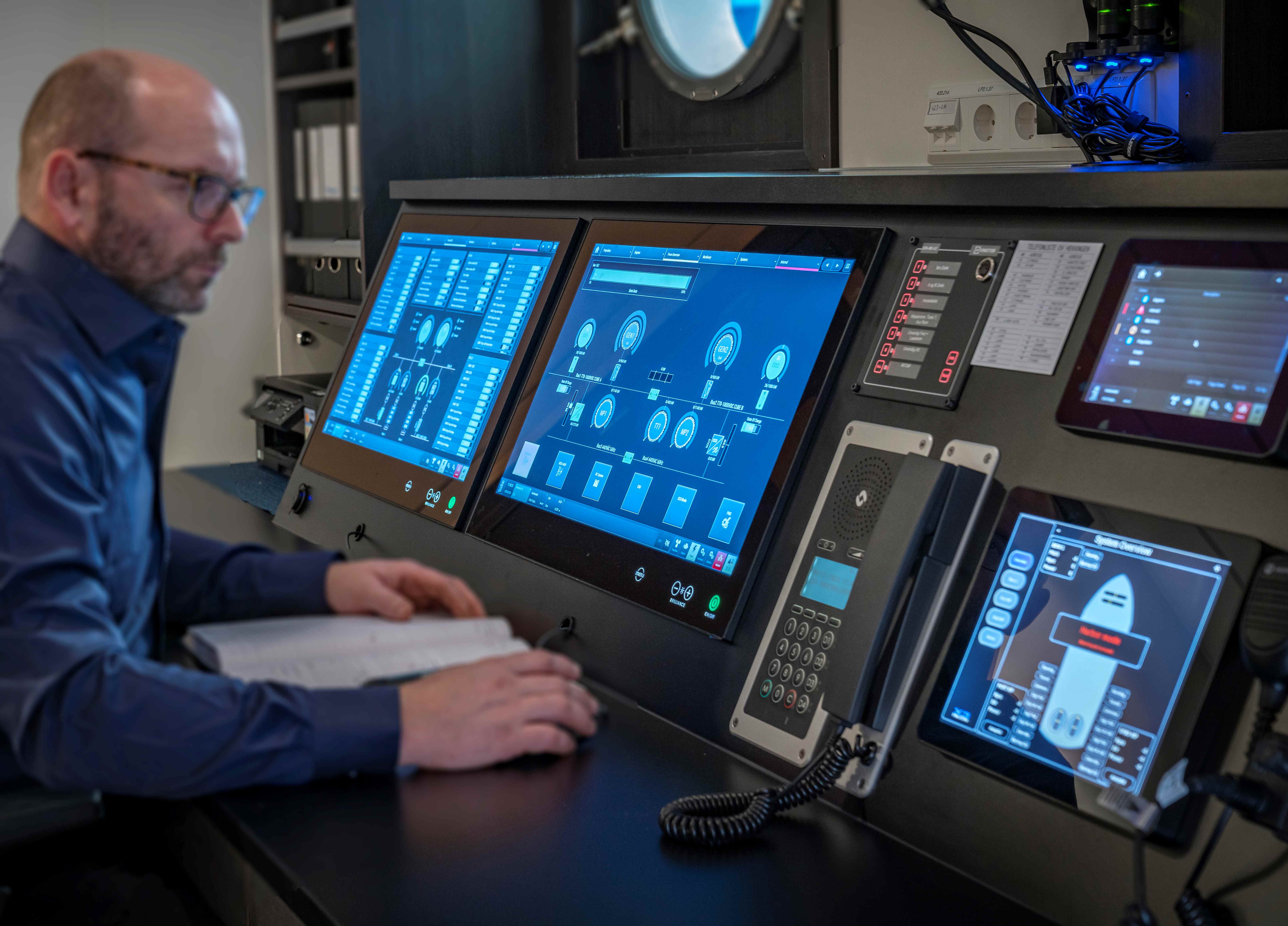 Operator monitoring marine systems on multiple digital control screens in a control room