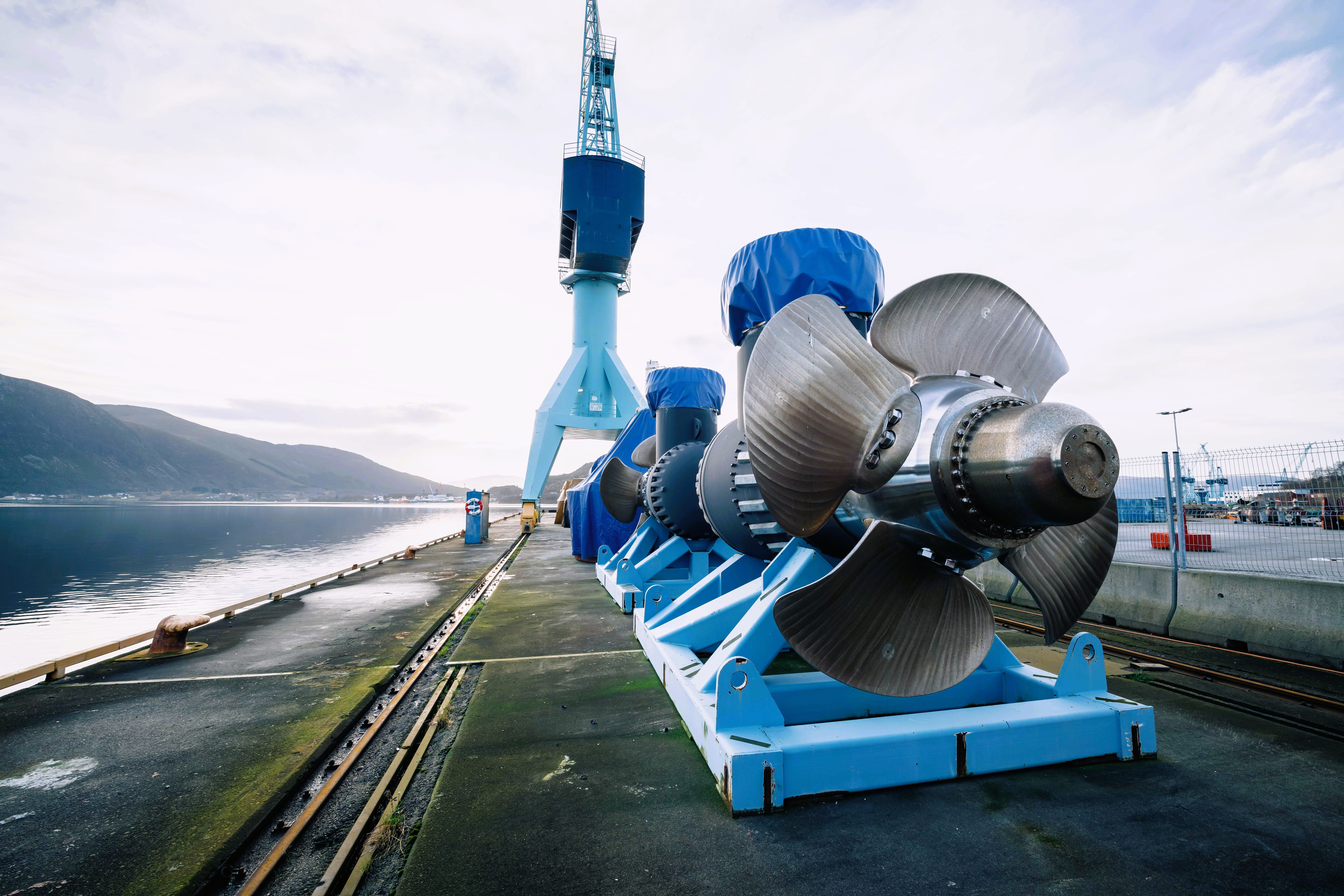 Two tunnel thrusters at quay side on blue transport frame, with a crane and waterfront in the background