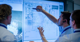 Engineers reviewing a technical system diagram on a digital screen, pointing at detailed design schematics