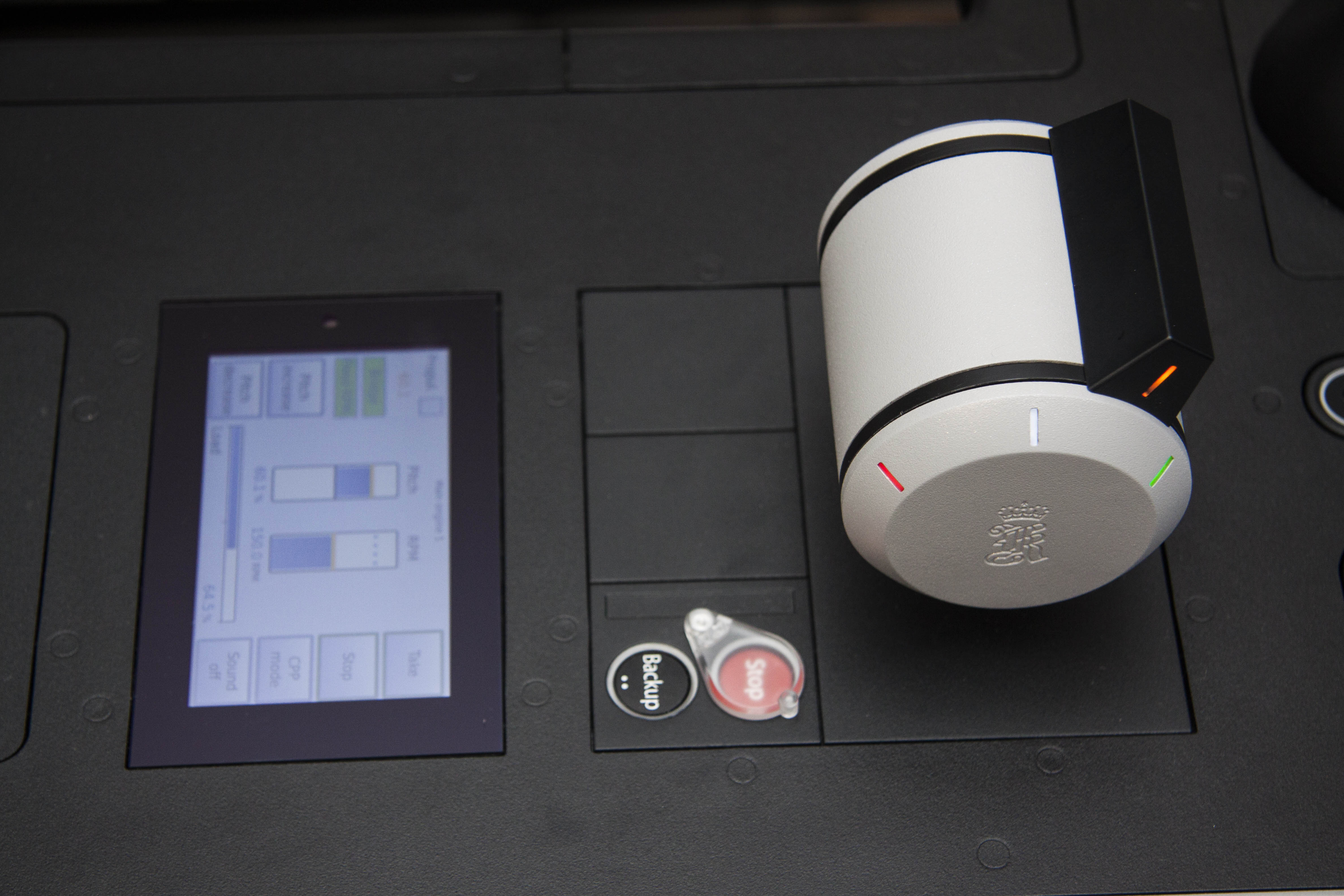 Close-up of a modern control panel featuring a cylindrical rotary knob with colored indicator lights, next to a small touchscreen displaying system controls