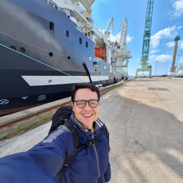 Person taking a selfie at a dock beside a large industrial vessel